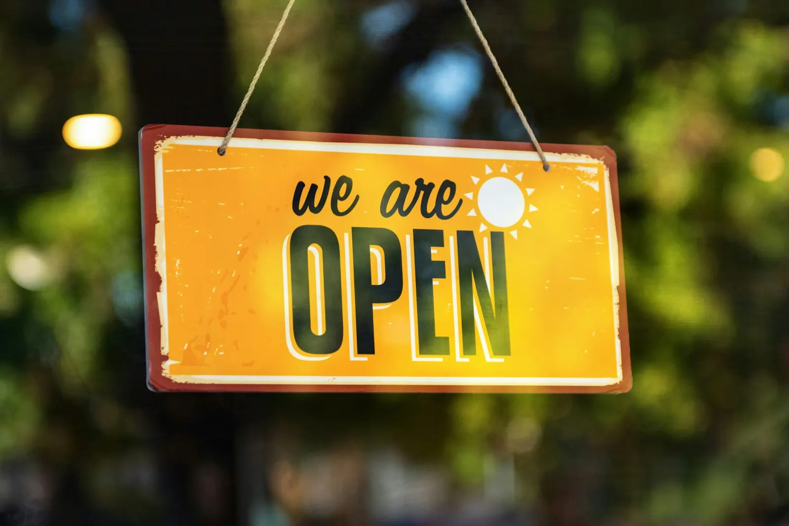 Žuta viseća tabla s natpisom We are open na staklenim vratima lokala